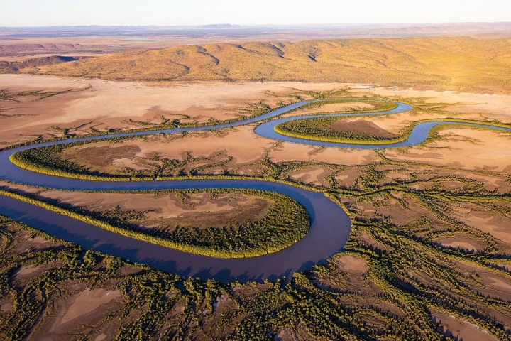 Aerial view of a winding river through a dry, brown landscape with scattered green vegetation.