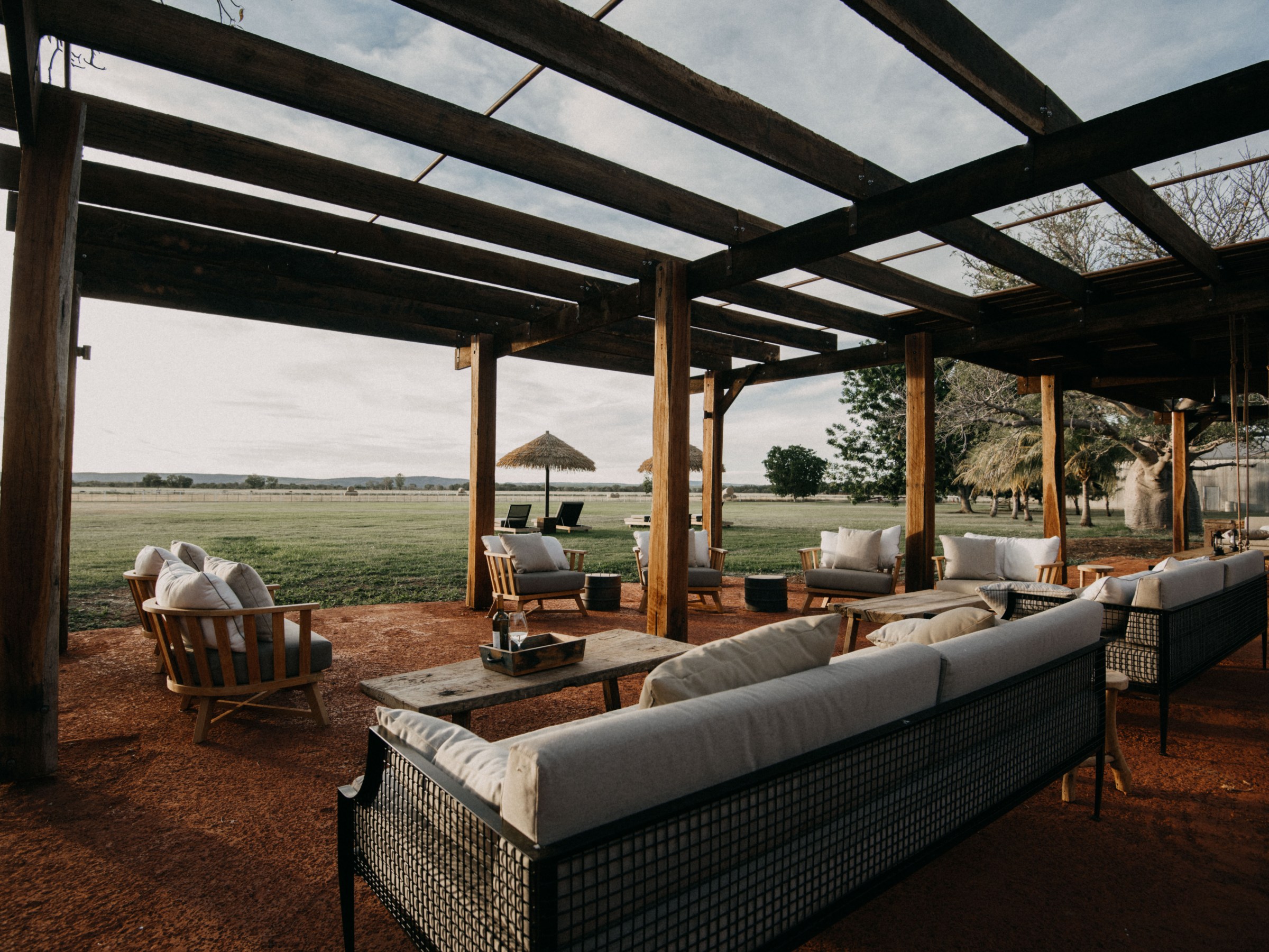Outdoor seating area under wooden pergola overlooking a grassy field.
