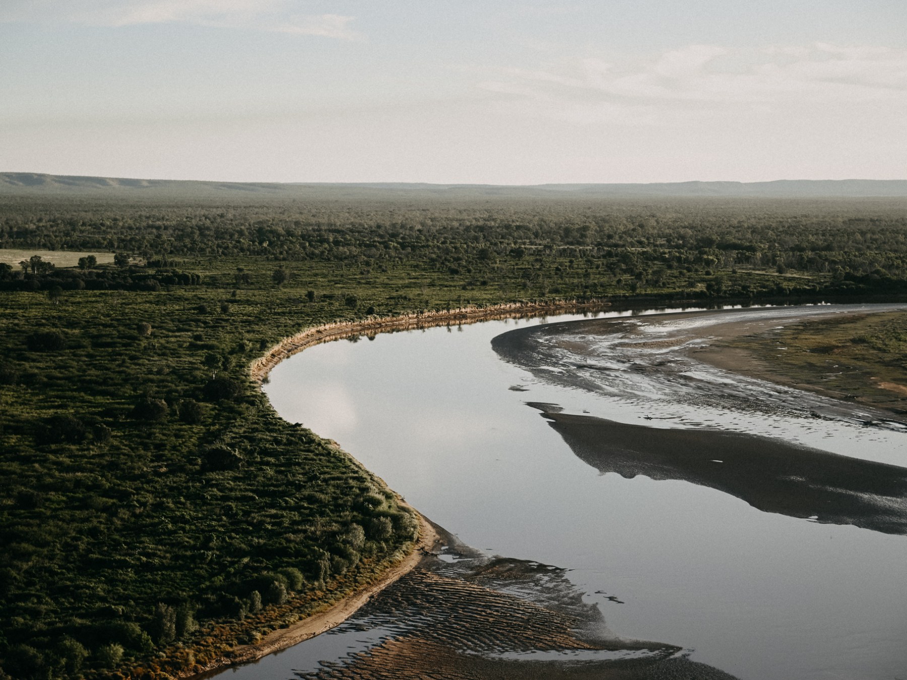 Aerial view of a river winding through a lush green forest and open landscape.