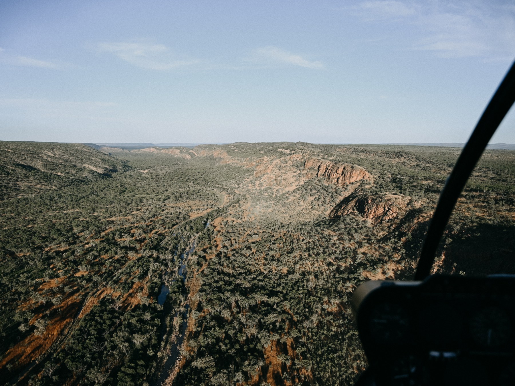 Aerial view of a rugged landscape with green vegetation and distant hills.