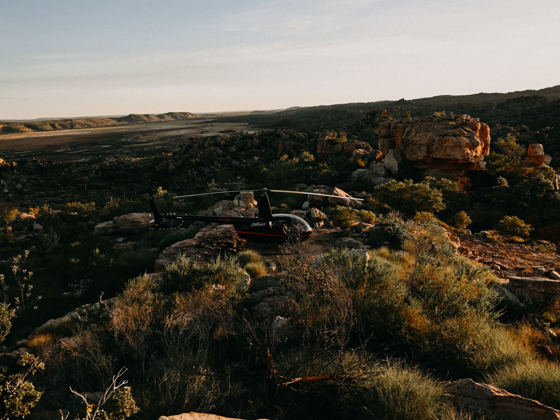 Helicopter landed in a rocky desert landscape at sunset.