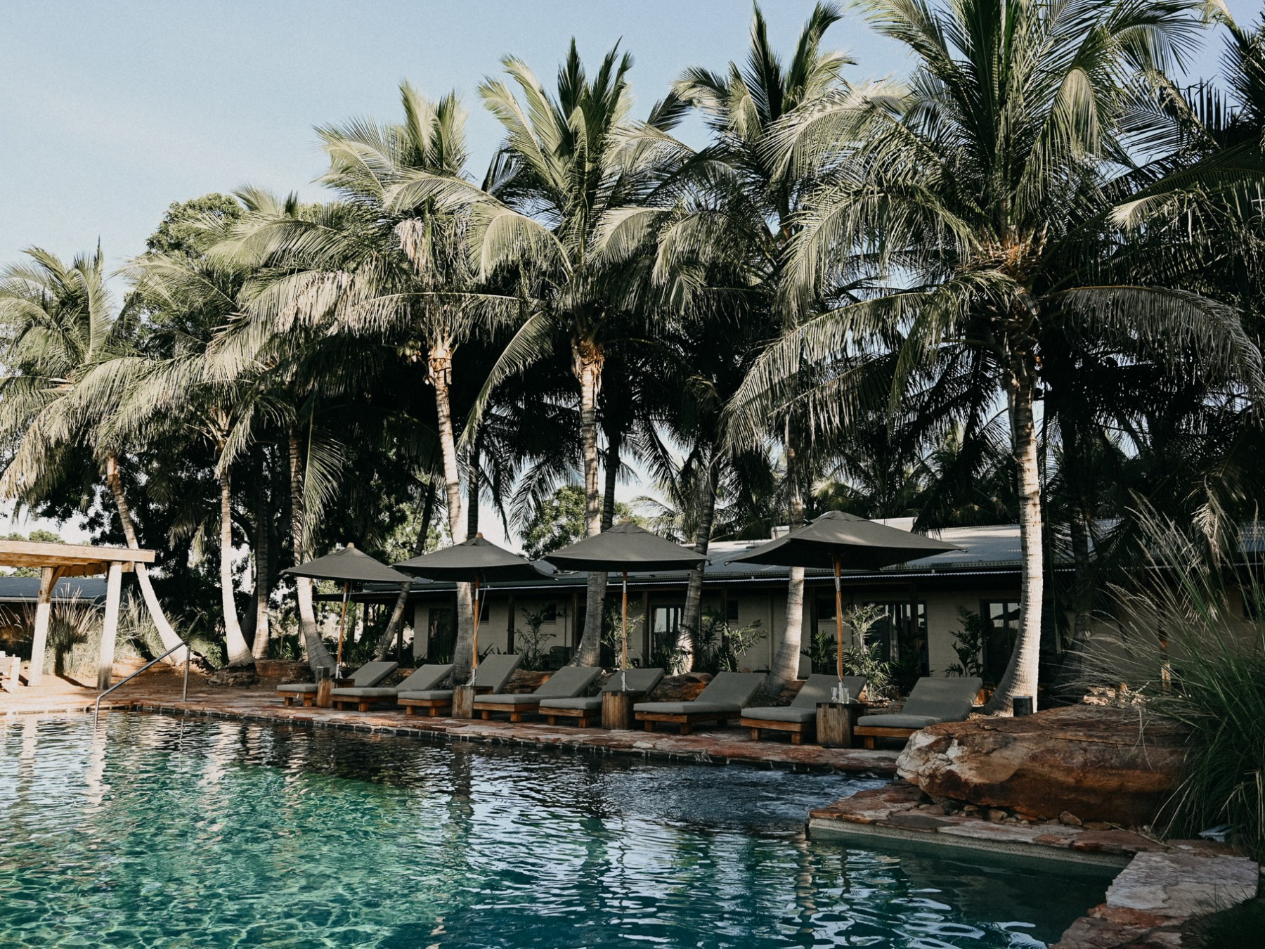 Palm trees and lounge chairs by a pool with cabanas.