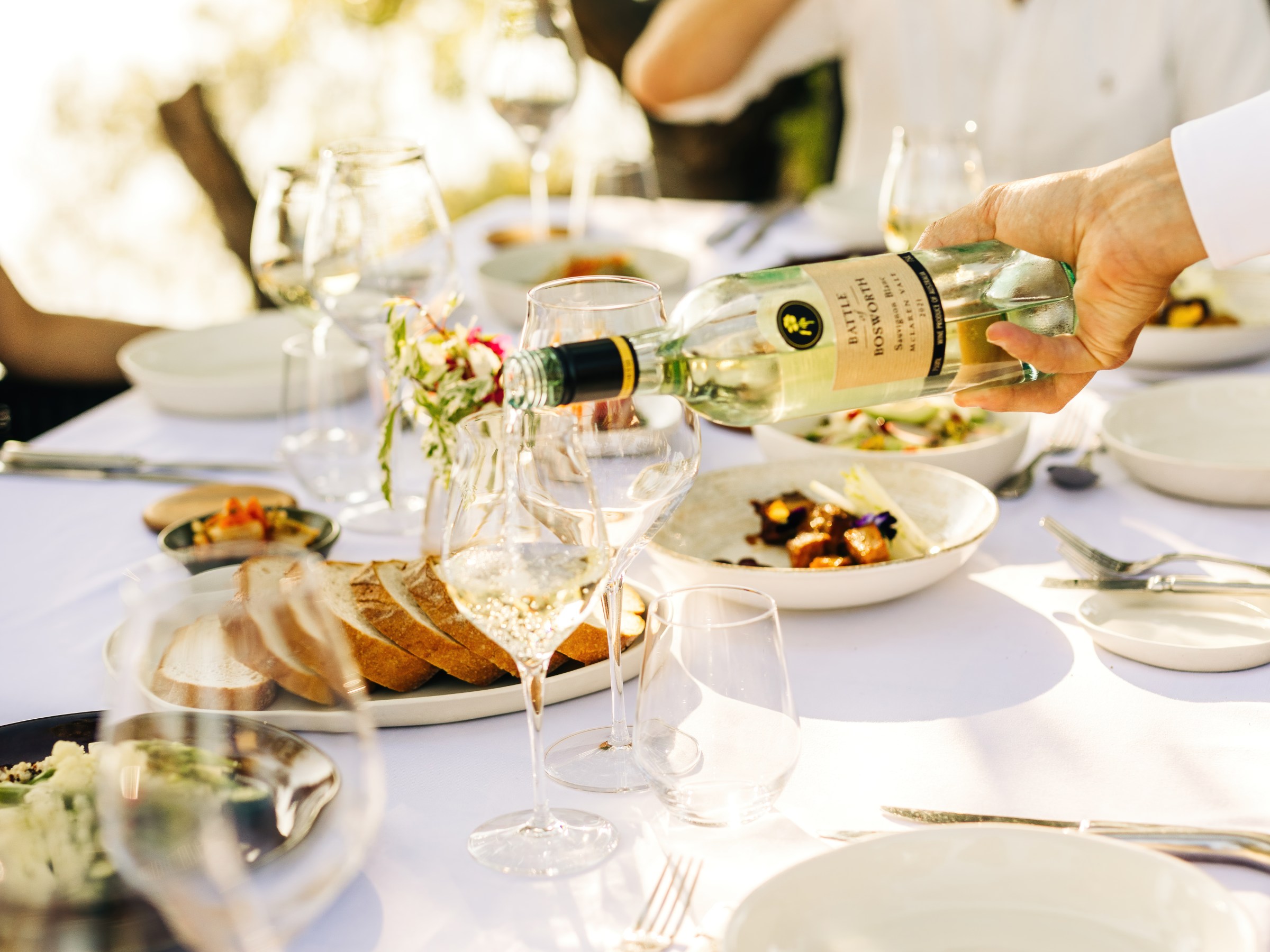 Outdoor dining table with wine, plates, and a person drinking