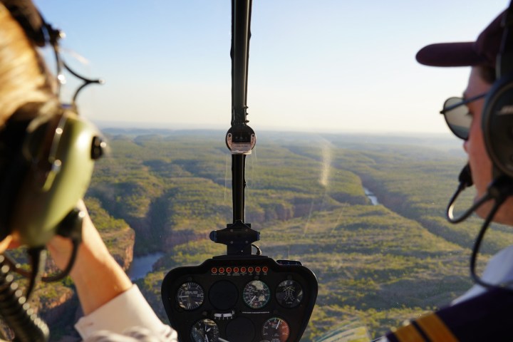 Helicopter cockpit view over scenic landscape with river and hills.
