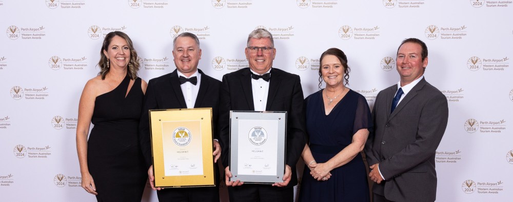 Group of five people in formal attire holding awards, posing against a branded backdrop.