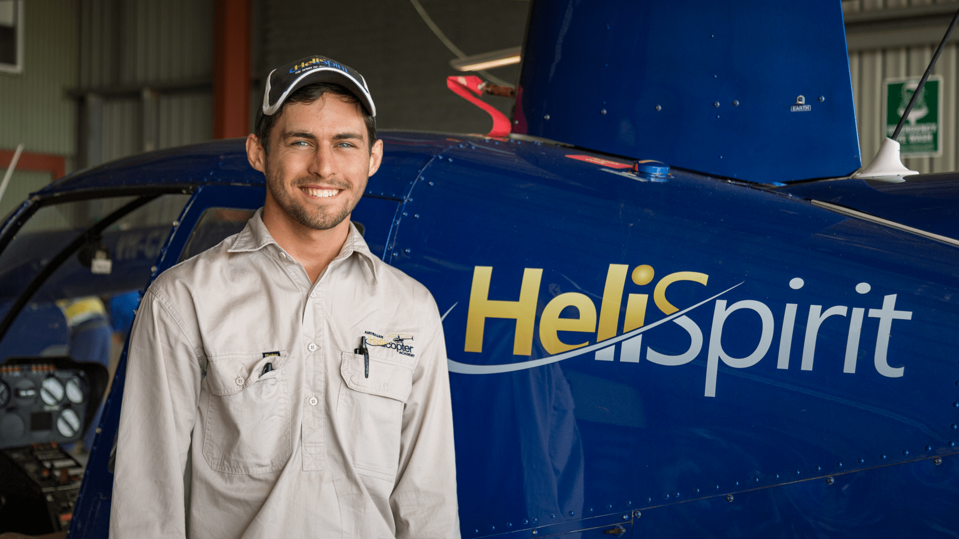 Man in uniform smiling in front of a blue helicopter indoors.