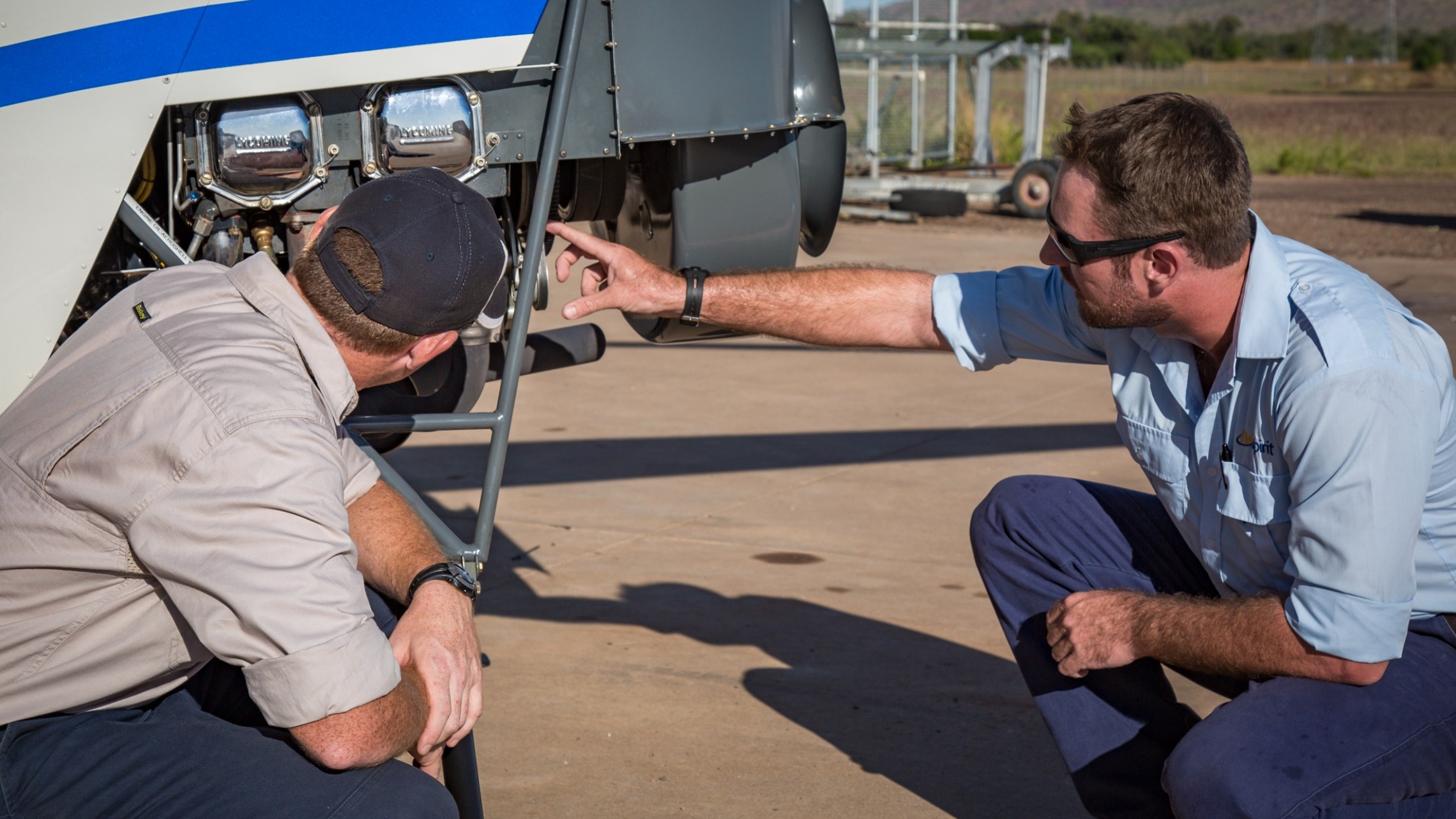 Two men inspecting an aircraft engine on a sunny day.