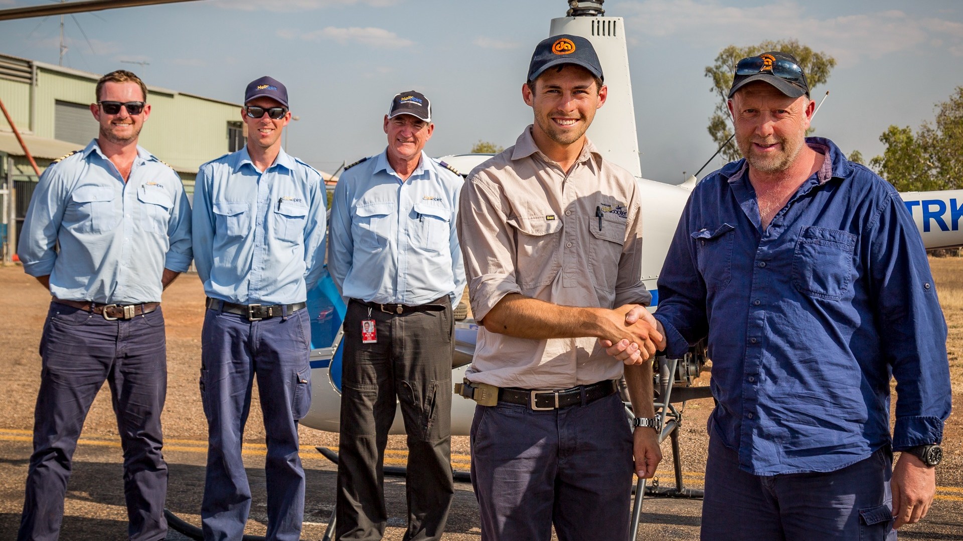 Five men in uniforms stand in front of a helicopter, with two shaking hands.