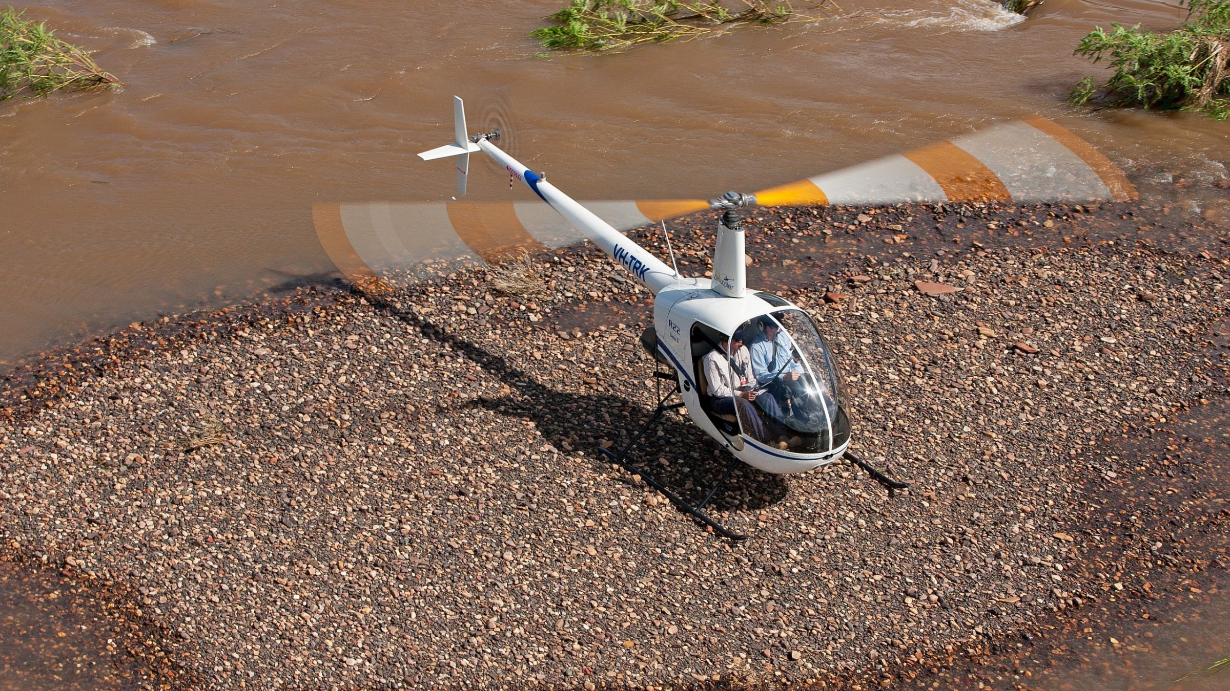 Helicopter on gravel island in a muddy river.