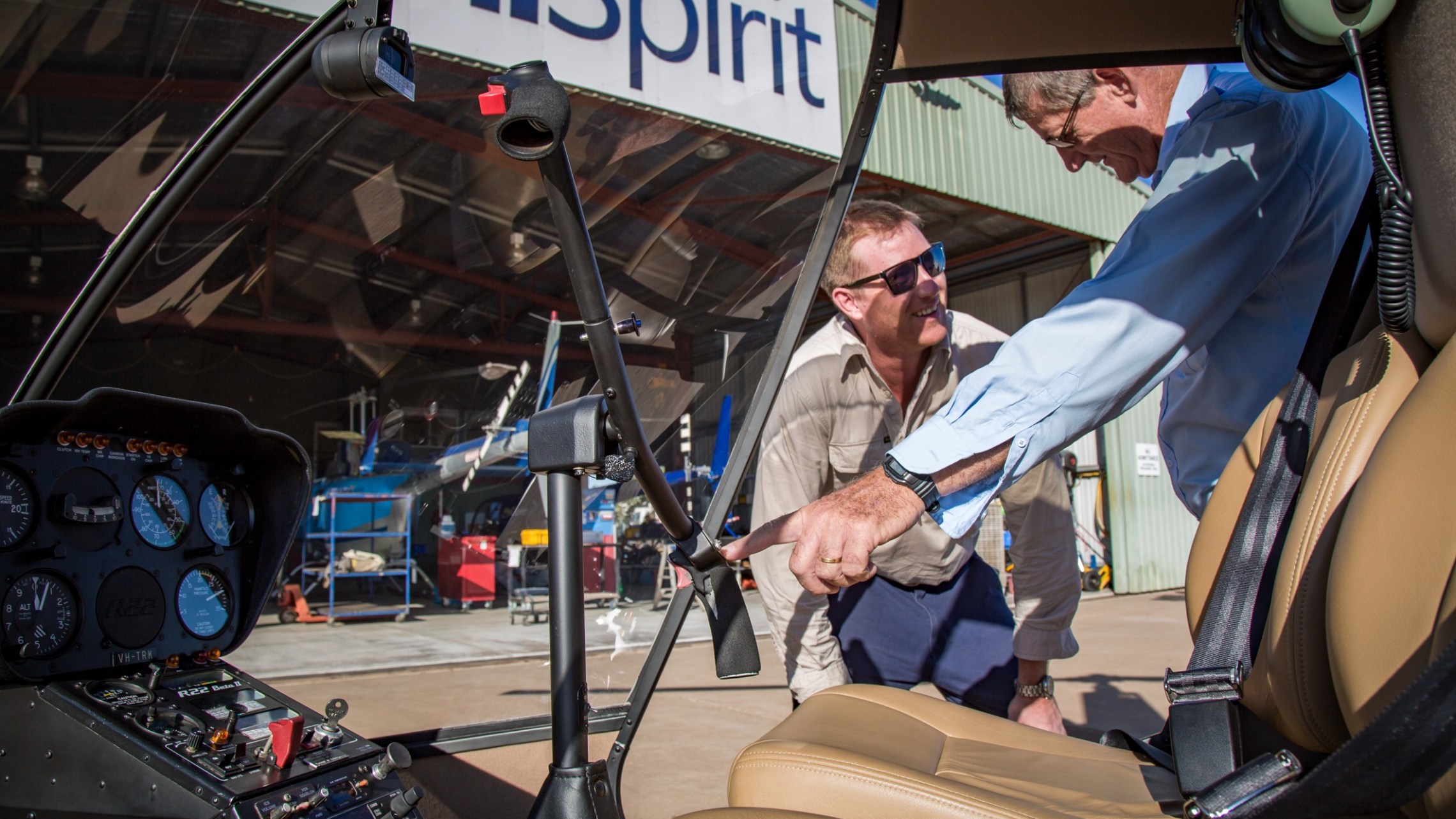 Two men inspecting a helicopter cockpit in a hangar.